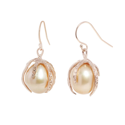 A pair of gold drop earrings featuring large, lustrous baroque pearls nestled in textured, claw-like gold settings, shown against a plain white background.