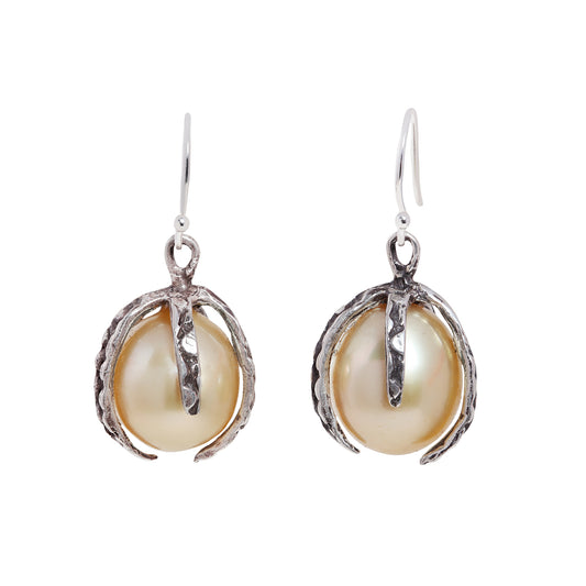 A pair of darkened silver drop earrings featuring large, lustrous baroque pearls nestled in textured, claw-like settings, shown against a plain white background.