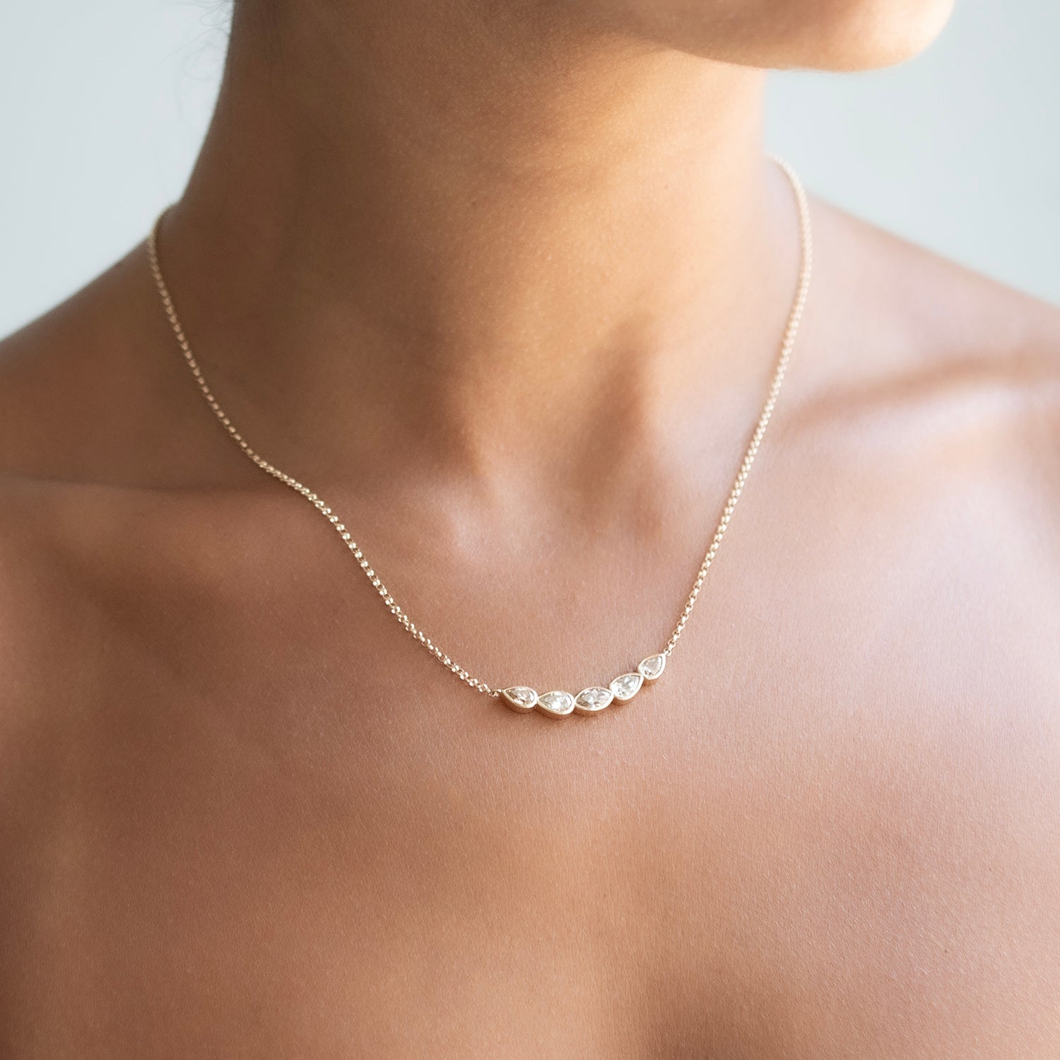 A delicate gold chain necklace with five small, irregularly shaped clear diamonds, shown worn on a model's neck.