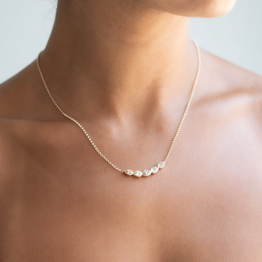 A delicate gold chain necklace with five small, irregularly shaped clear diamonds, shown worn on a model's neck.