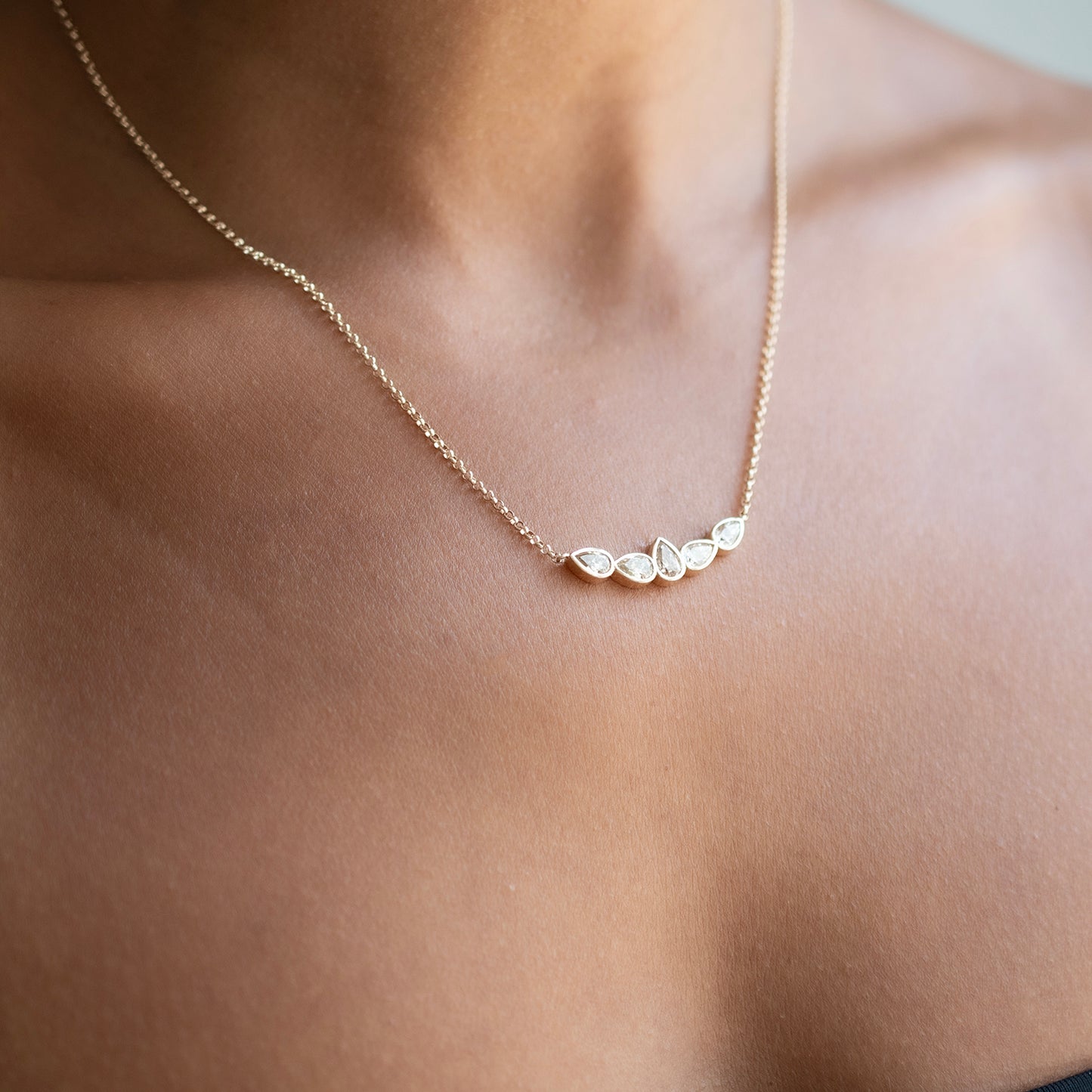A delicate gold chain necklace with five small champagne diamonds worn on a model's neck.