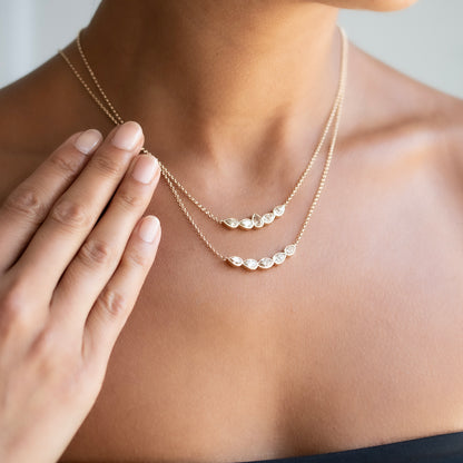 A delicate gold chain necklace with five small, irregularly shaped clear diamonds, shown worn on a model's neck.