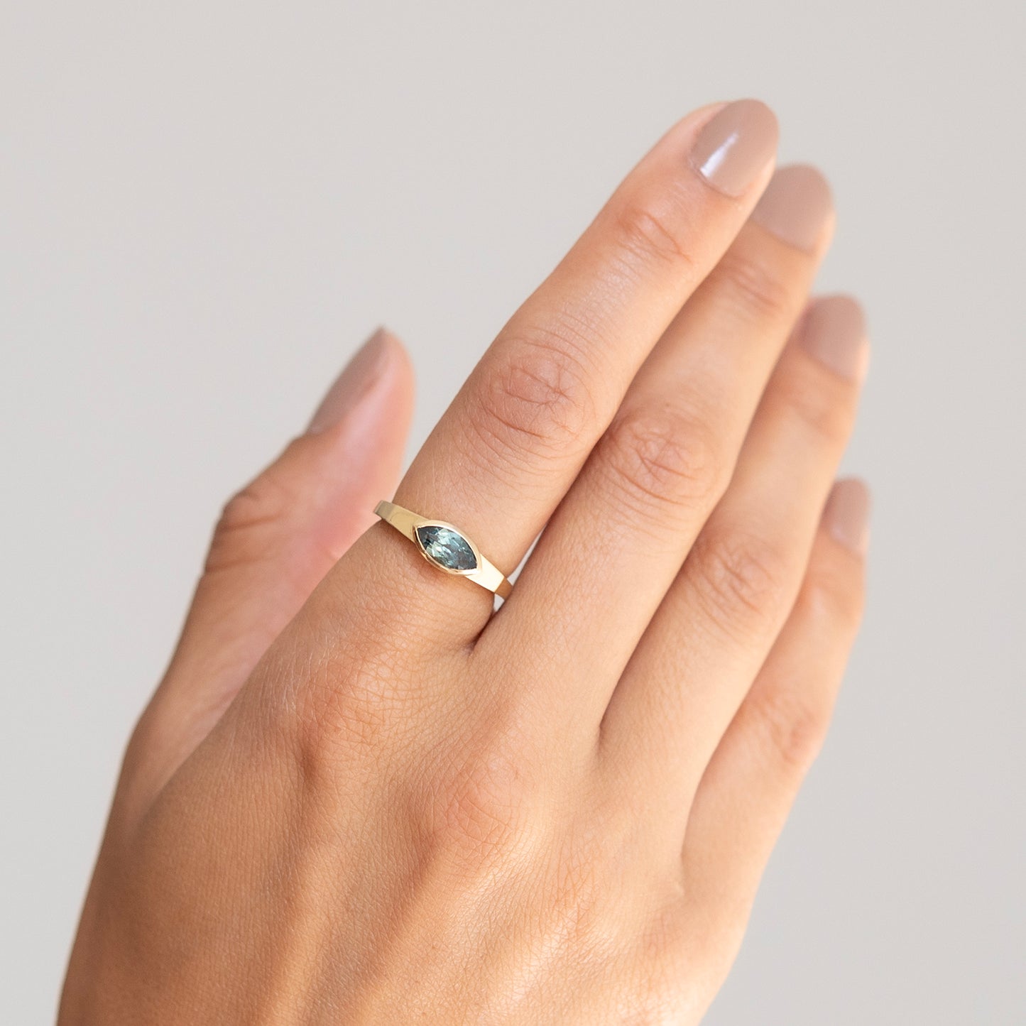 Hand wearing a gold ring with a green gemstone on a neutral background