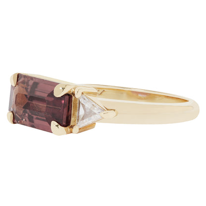 Gold ring with a rectangular purple gemstone and a triangular clear gemstone on a white background