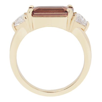 Gold ring with a central maroon gemstone and two smaller clear stones on a white background