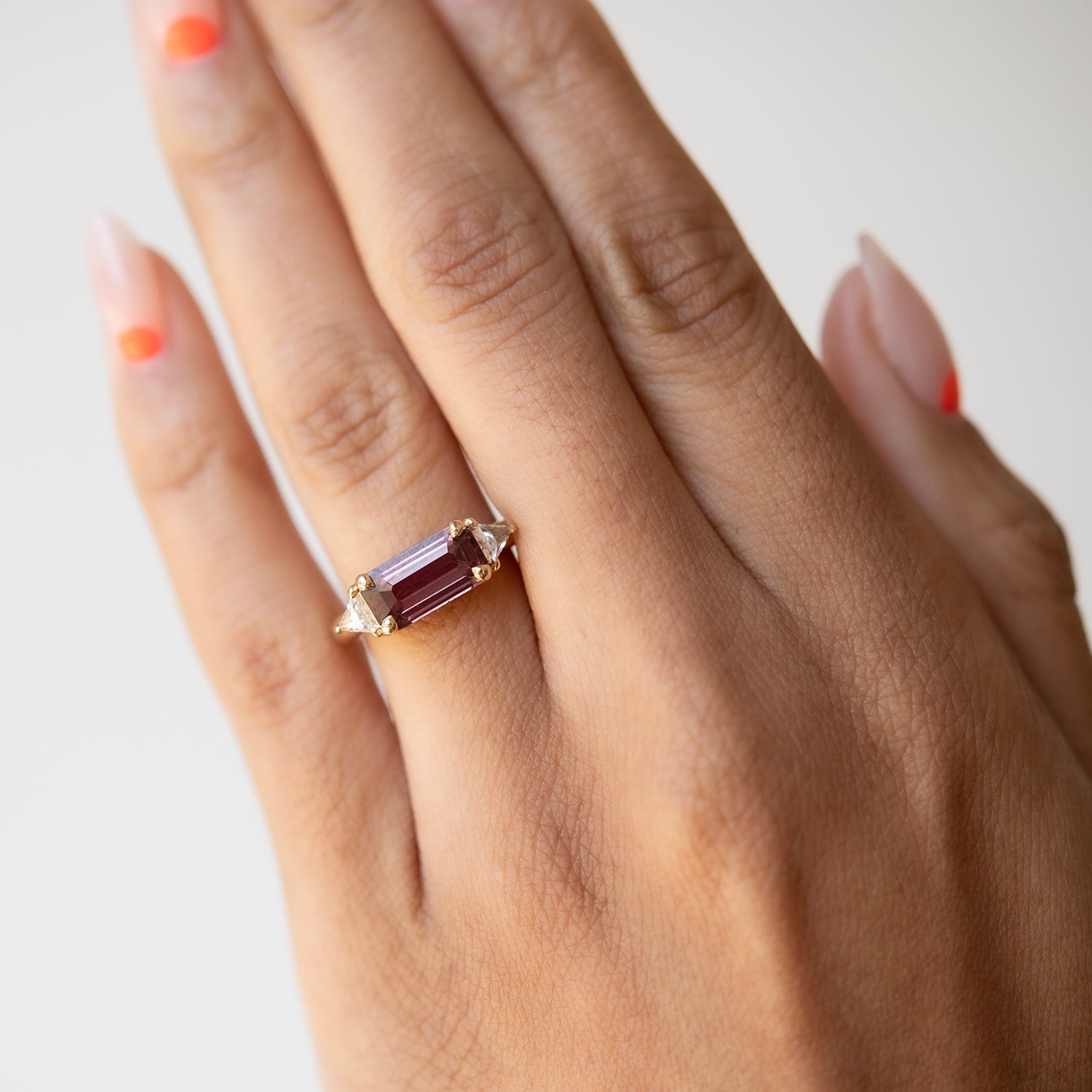 Hand wearing a ring with a purple gemstone on a light background
