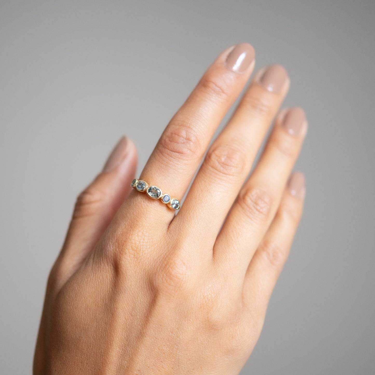Hand wearing a ring with five stones on a neutral background