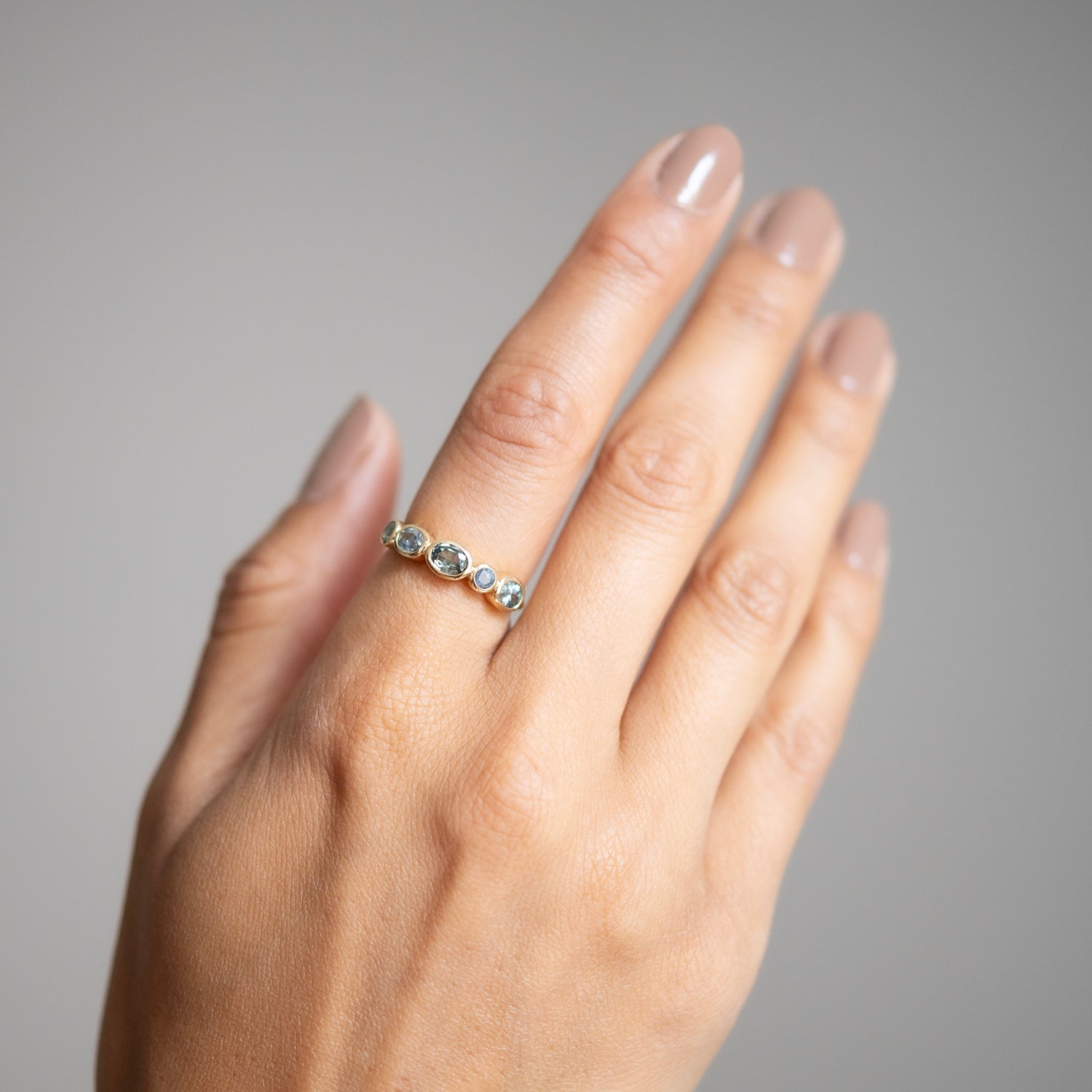Hand wearing a ring with five stones on a neutral background
