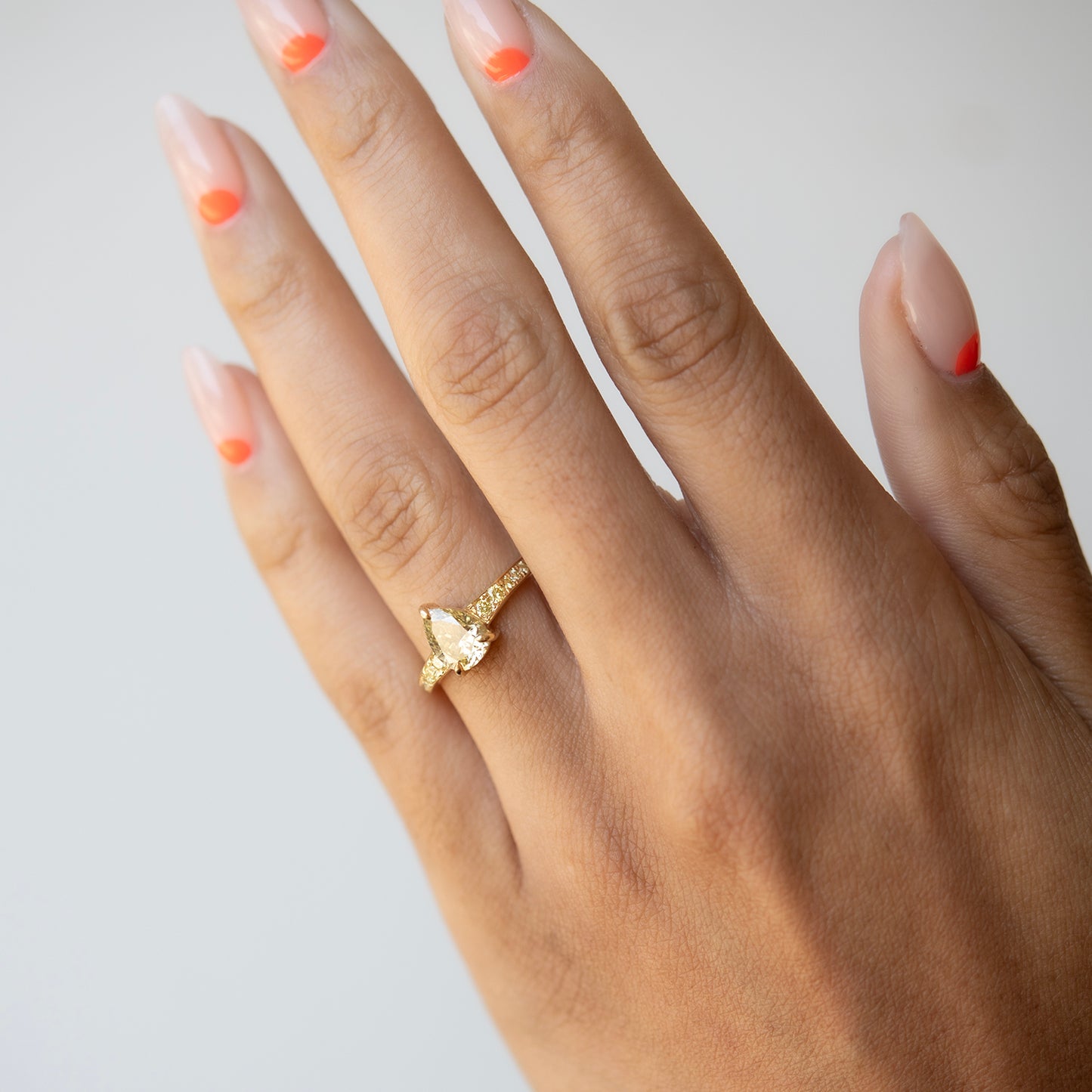 Hand wearing a gold ring with a pear-shaped gemstone on a light background