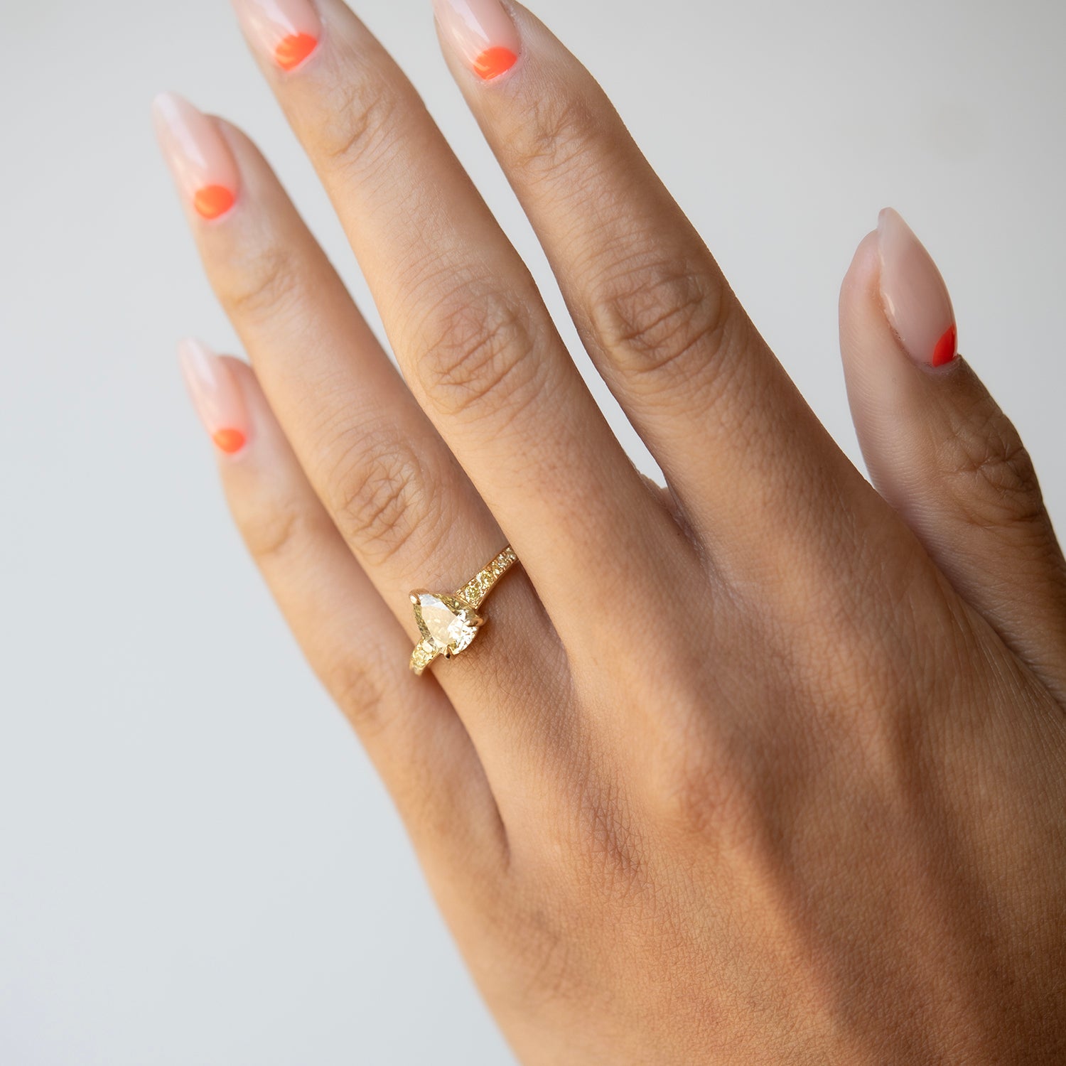 Hand wearing a gold ring with a pear-shaped gemstone on a light background
