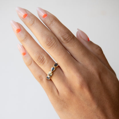 Hand wearing a gold ring with three stones on a plain background