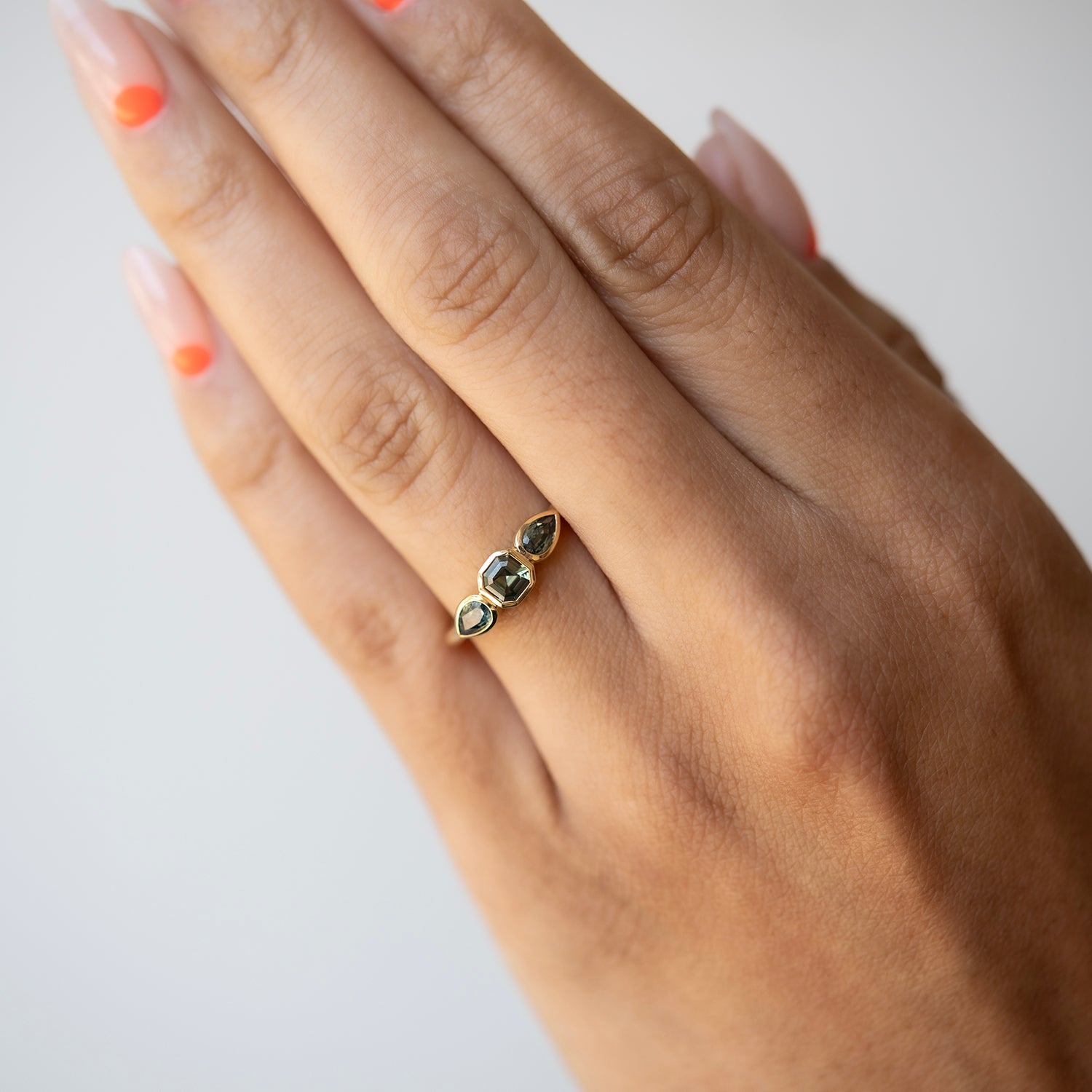 Hand wearing a gold ring with gemstones on a plain background