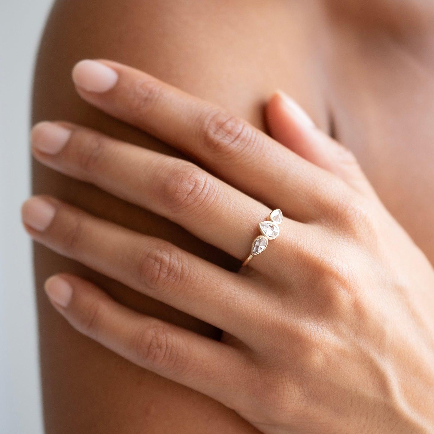 A close-up lifestyle shot of a delicate silver ring with three marquise-cut clear stones set in a leaf-like cluster, worn on a person's ring finger.