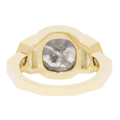 A gold signet-style ring featuring a large, rough-cut, cushion-cut gray gemstone in a polished gold bezel setting, shown on a solid white background.