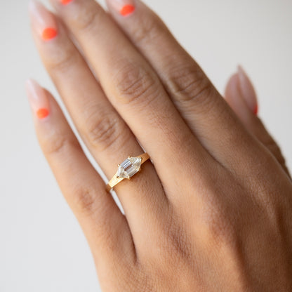 Hand wearing a gold ring with a clear gemstone on a light background