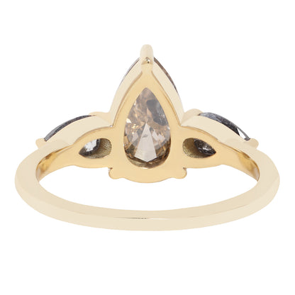 A gold ring featuring a large pear-cut clear diamond with inclusions, accented by two smaller marquise-cut gray diamonds on either side, shown on a plain white background.