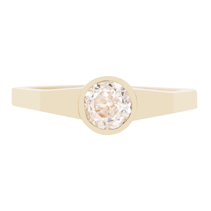 A minimalist yellow gold ring featuring a bezel-set round-cut clear diamond, presented on a solid white background.