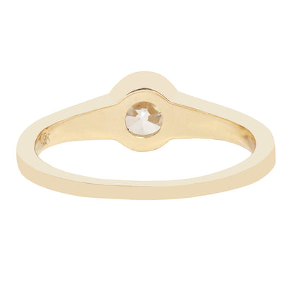 A minimalist yellow gold ring featuring a bezel-set round-cut clear diamond, presented on a solid white background.
