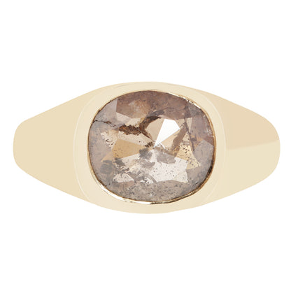 A signet-style ring with a wide, smooth champagne-gold band and a large, cushion-cut rough diamond center stone showing brown, gray, and white crystalline inclusions.