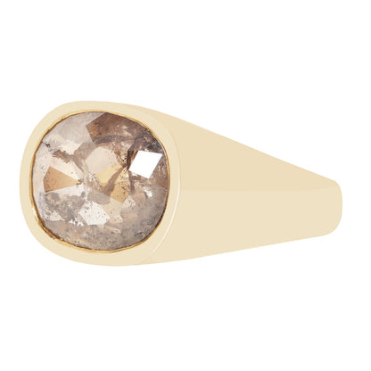 A signet-style ring with a wide, smooth champagne-gold band and a large, cushion-cut rough diamond center stone showing brown, gray, and white crystalline inclusions.