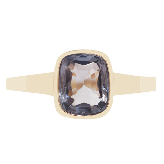 Bezel set solitaire yellow gold ring with a dark blue spinel rectangular stone on white background. 