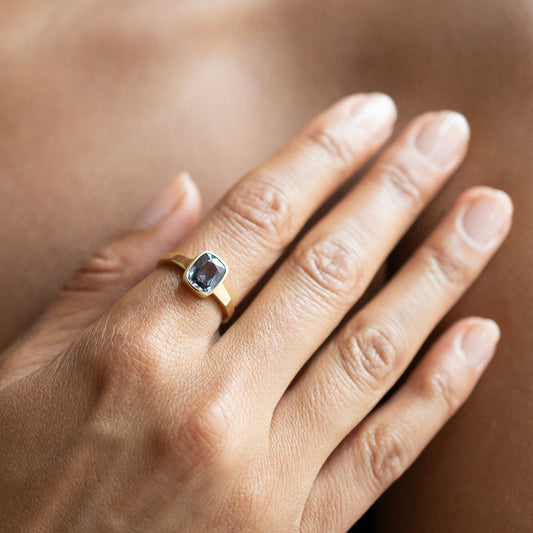 A close-up of a hand wearing a gold ring with a rectangular blue gemstone.