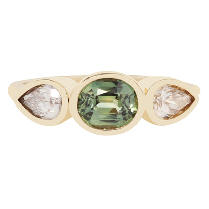 A gold ring featuring a central oval green gemstone flanked by two pear-cut clear stones, set against a plain white background.