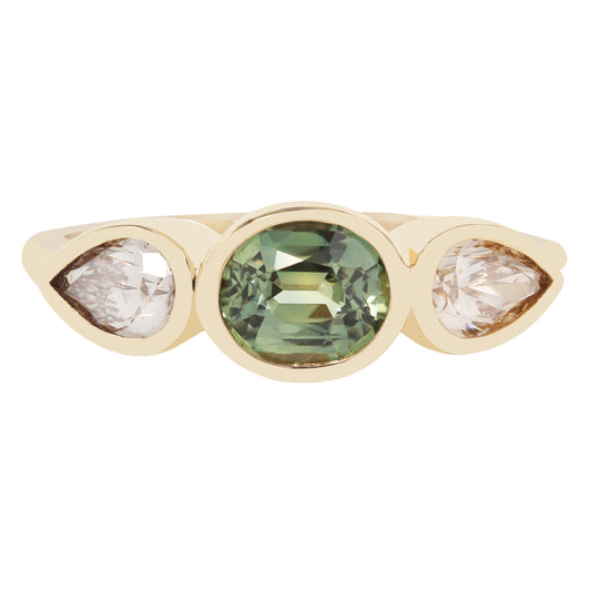 A gold ring featuring a central oval green gemstone flanked by two pear-cut clear stones, set against a plain white background.