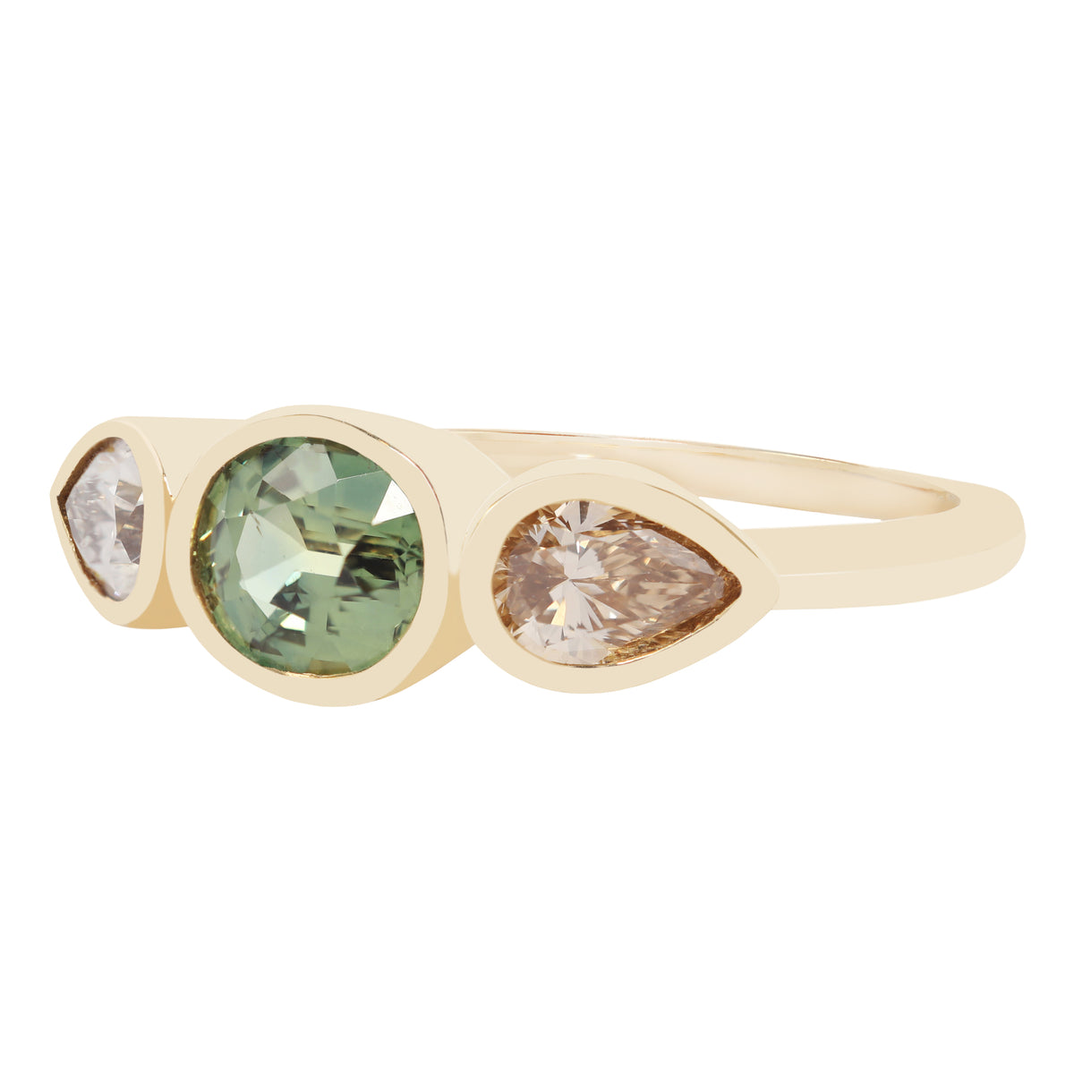 A gold ring featuring three bezel-set teardrop-shaped gemstones: a central light green oval stone, flanked by a small clear round stone on the left and a champagne pear-cut stone on the right, set against a plain white background.