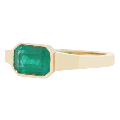 A yellow gold ring featuring a large, faceted emerald-cut green gemstone in a bezel setting, shown against a plain white background.