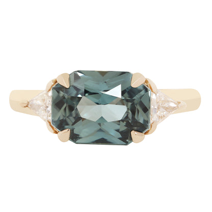 An emerald-cut blue sapphire ring set in a yellow gold four-prong setting with small round and marquise-cut side diamonds, shown against a plain white background.