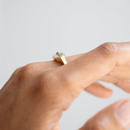 A close-up of a hand wearing a minimalist gold ring with a faceted clear gemstone, set against a soft, light gray background.