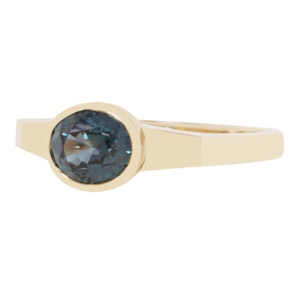 A yellow gold ring featuring a bezel-set oval faceted dark blue gemstone, shown against a plain white background.