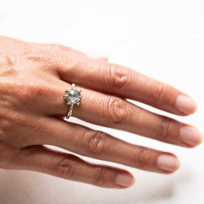 A close-up of a hand wearing a white gold ring with a large gray round gemstone, set against a plain white background.