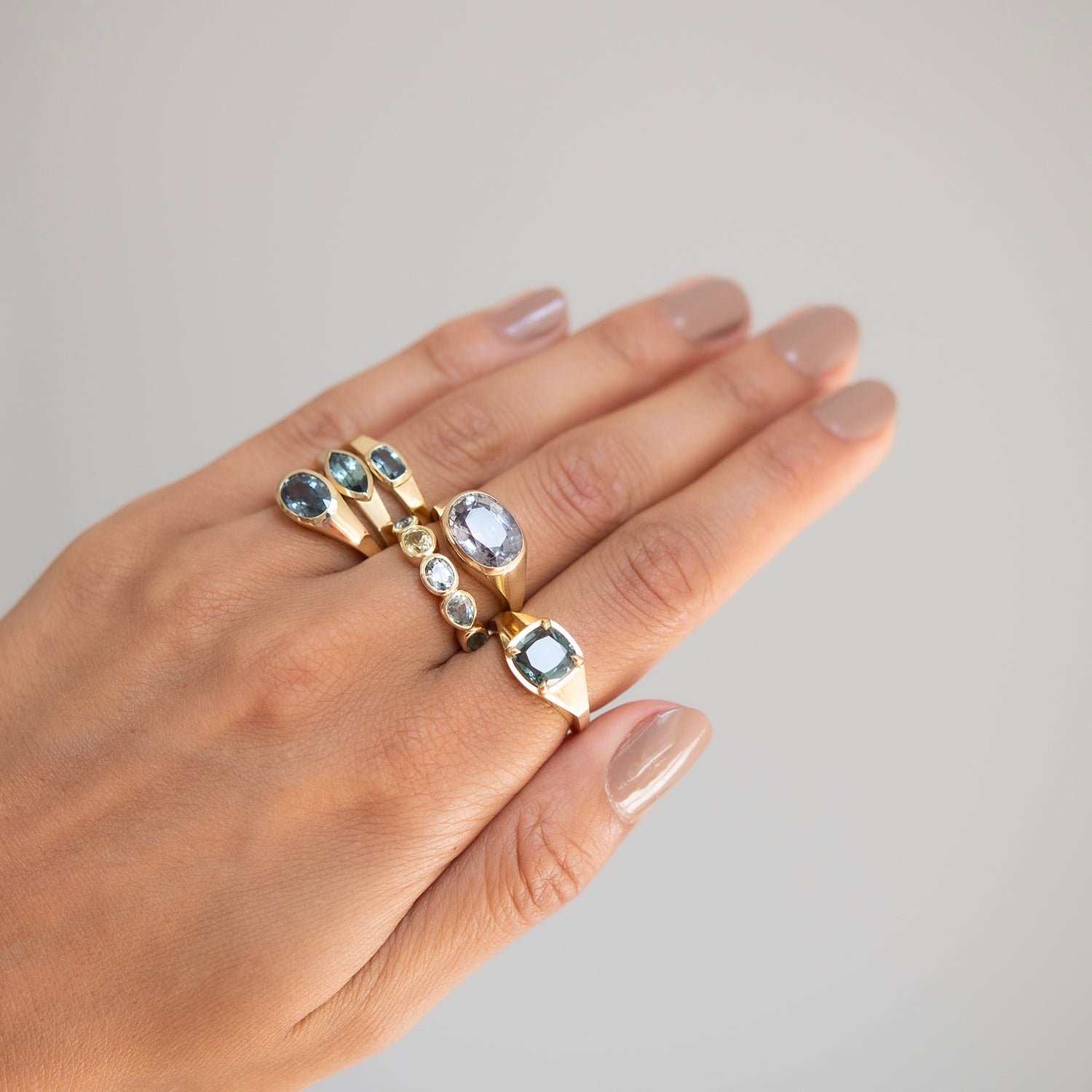 Lauren Wolf - Hand wearing multiple gold rings with gemstones on a neutral background