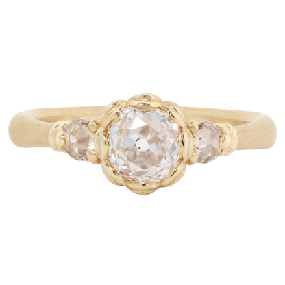 A gold ring featuring a large, round-cut clear gemstone surrounded by a decorative border of small gold beads, set on a smooth gold band against a plain white background.