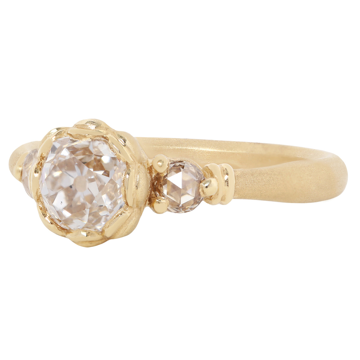 A gold ring featuring a large, round-cut clear gemstone surrounded by a decorative border of small gold beads, set on a smooth gold band against a plain white background.