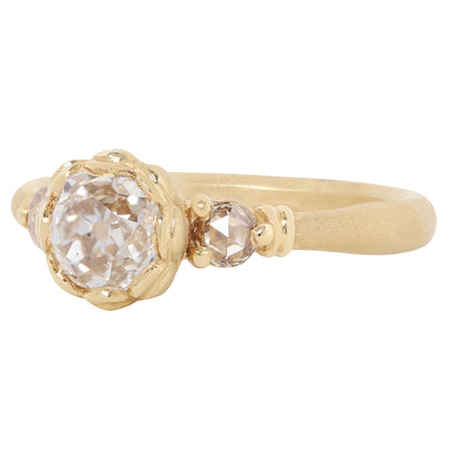 A gold ring featuring a large, round-cut clear gemstone surrounded by a decorative border of small gold beads, set on a smooth gold band against a plain white background.