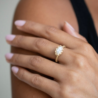 A gold ring with a large oval clear gemstone set on a person's ring finger, shown close-up on their hand.