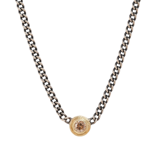 A silver-toned curb chain necklace featuring a small circular gold-toned pendant with a clear faceted gemstone, shown against a plain white background.