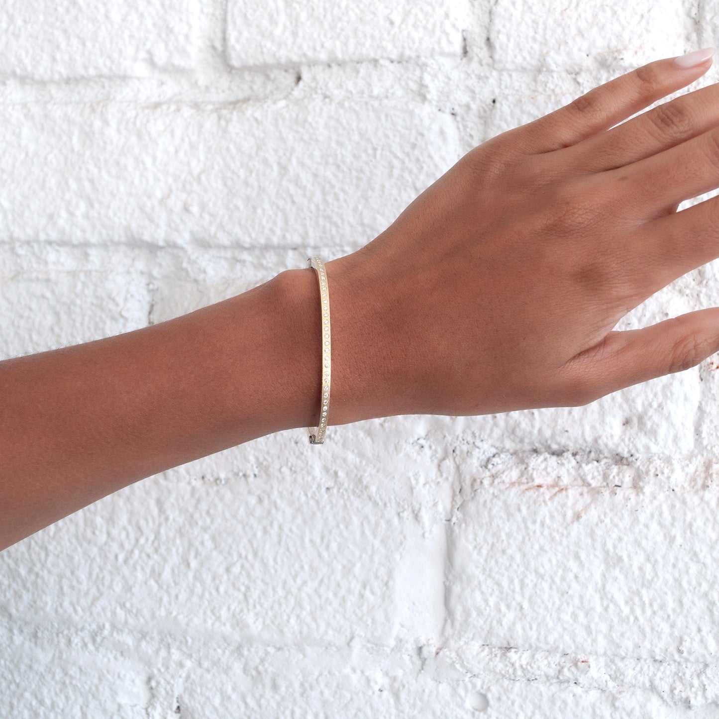 Rene Escobar - Hand wearing a gold bracelet against a textured white background