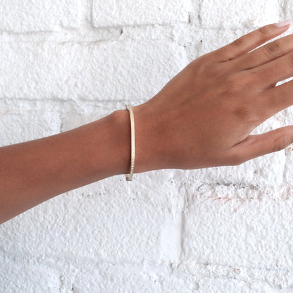 Rene Escobar - Hand wearing a gold bracelet against a textured white background