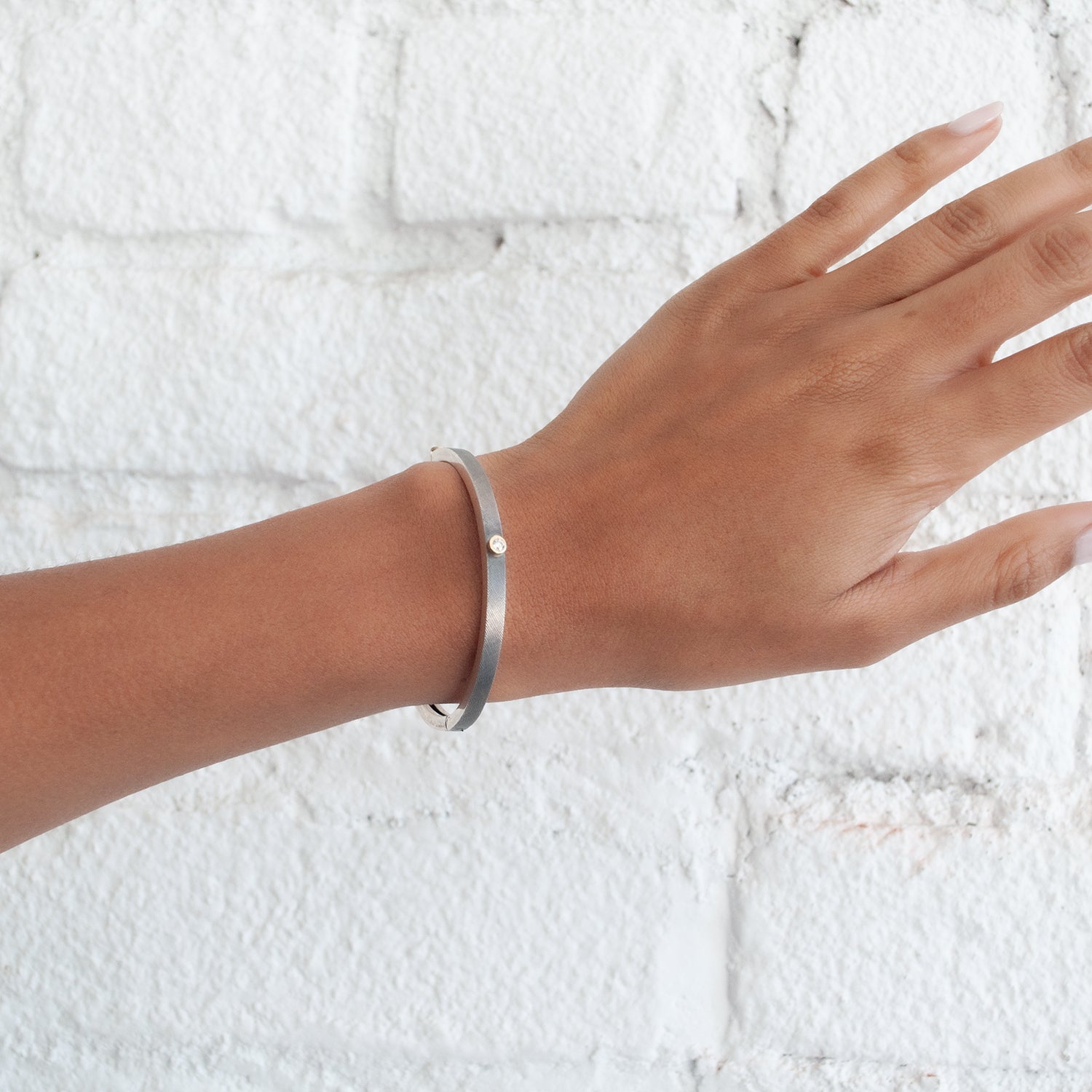 Rene Escobar - Hand wearing a silver bracelet on a textured white background
