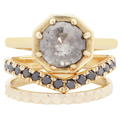 A stack of three gold rings on a white background. The top ring features an octagonal bezel-set gray gemstone.