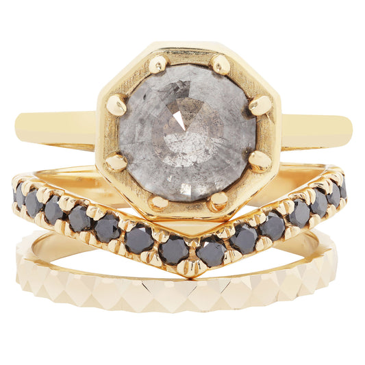 A stack of three gold rings on a white background. The top ring features an octagonal bezel-set gray gemstone.
