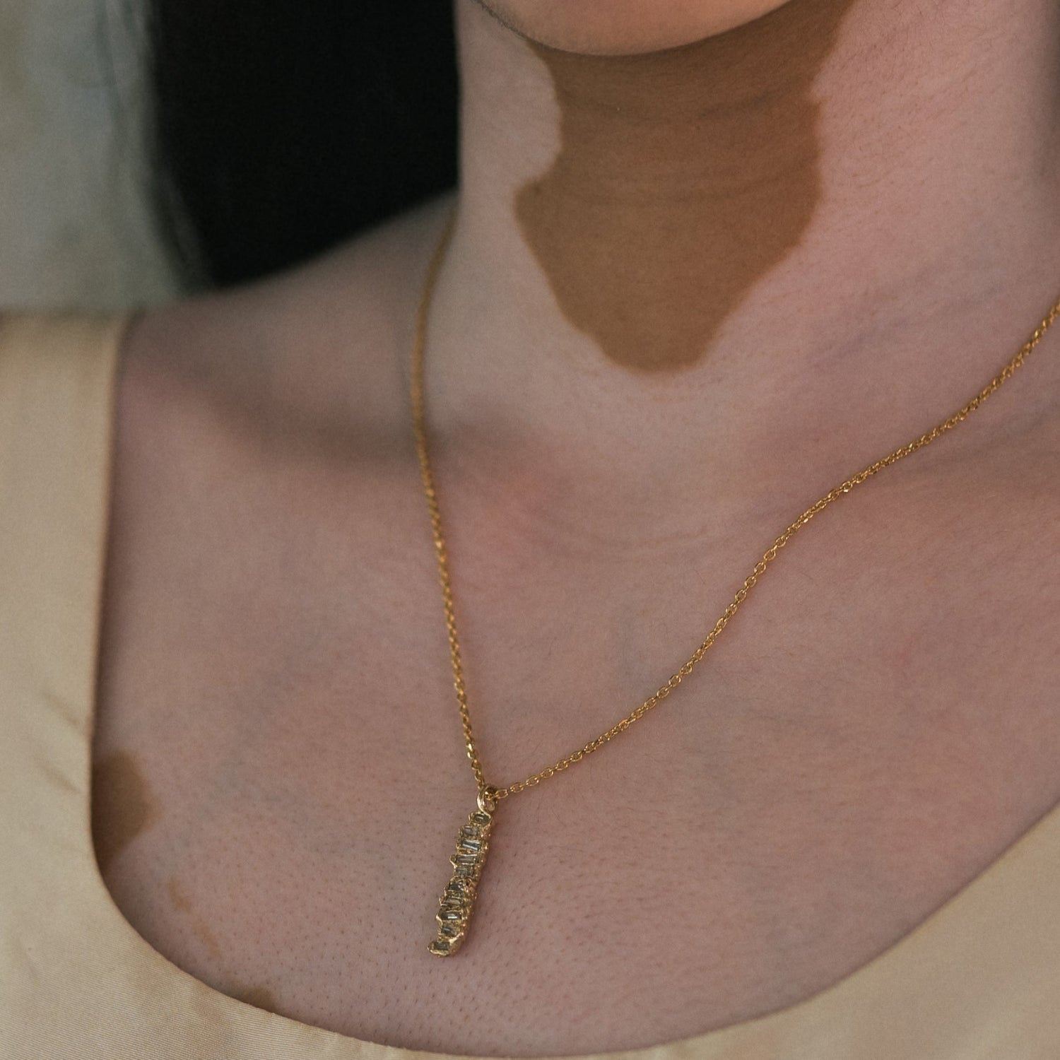 Ellis Mhairi Cameron - Gold necklace with a pendant on a person wearing a beige top.