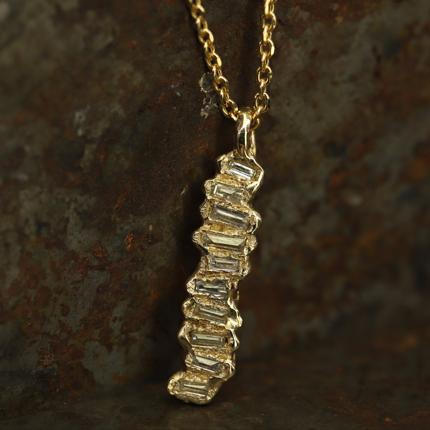 Ellis Mhairi Cameron - Gold necklace with a diamond pendant on a textured brown background