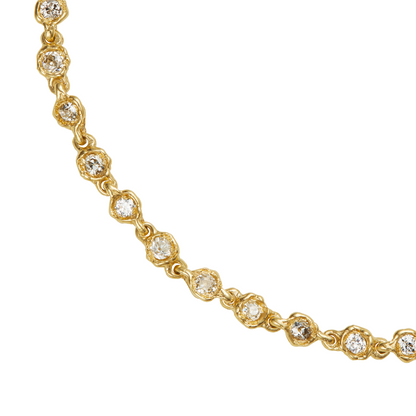 A close-up of a gold tennis necklace featuring small clear round-cut stones in each link, set against a plain white background.