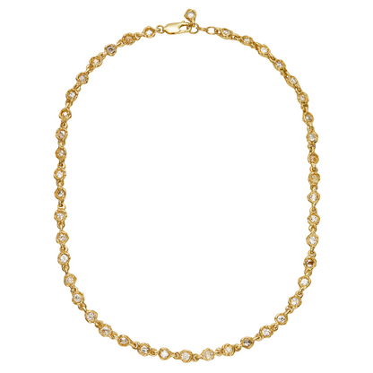 A gold tennis necklace with small clear gemstones set in each link, arranged in an oval shape on a plain white background.