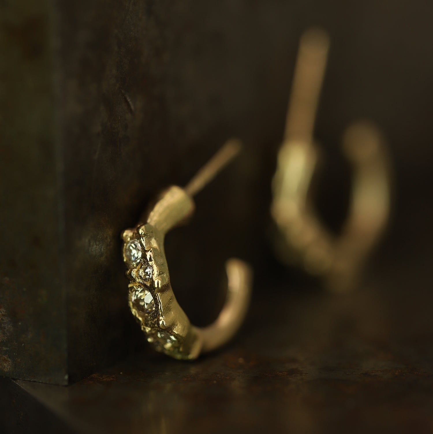 Ellis Mhairi Cameron - Gold hoop earrings with embedded stones on a dark surface